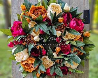 May include: A wreath made of faux peonies in shades of peach, cream, and pink, with green leaves. The wreath is hanging on a wooden door.