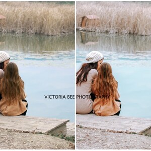 May include: Two people, a mother and daughter, are sitting on a wooden dock by a lake. They are wearing winter clothing, including hats and coats. The lake is calm and the water is a light blue color. The background is a blurry image of trees and reeds.