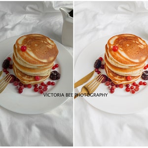 May include: A white plate with a stack of four golden brown pancakes topped with red berries. The plate is on a white surface with two gold forks and a white pitcher.