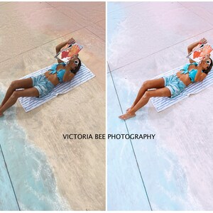 May include: A woman wearing a blue bikini top and denim shorts lies on a white towel on a painted beach scene. She is reading a magazine and the text "VICTORIA BEE PHOTOGRAPHY" is visible on the ground.