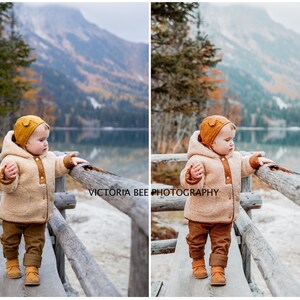 May include: A toddler wearing a brown and beige hooded jacket with a brown hat and brown pants stands on a wooden bridge overlooking a lake. The lake is surrounded by trees and mountains. The background is blurred.