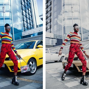 May include: A person wearing a rainbow striped sweater, red pants with a floral pattern, and black boots is walking down a city street. They are carrying a floral patterned handbag. A yellow car is parked behind them.