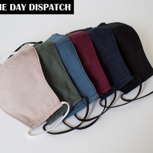 Puede incluir: Una colección de seis mascarillas de tela dispuestas en fila, con colores que incluyen beige, verde oliva, azul, burdeos, azul marino y negro. Cada mascarilla tiene una forma contorneada con costuras visibles y elásticos para las orejas.
