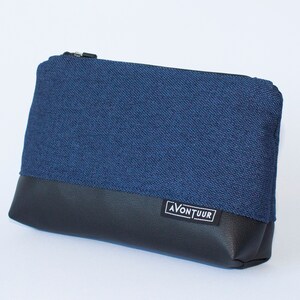 May include: A rectangular pouch with a navy blue fabric upper and a black leather-like bottom. The pouch has a black zipper closure and a small white label with the word "AVONTUUR" in black. The pouch is designed for carrying small items.