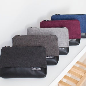 May include: A collection of five rectangular zippered pouches in various colors. The pouches feature a textured fabric upper and a black leather-like bottom. Each pouch has a small label that reads "AVONTUUR". Colors include black, gray, burgundy, and blue.