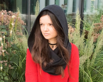 May include: A woman wearing a black hooded scarf over a red sweater. The scarf is made of a soft, drapey fabric and has a simple, elegant design.
