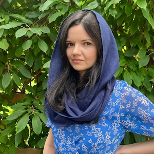 Könnte beinhalten: Ein dunkelblauer Kapuzenschal aus Leinen, der über Kopf und Schultern drapiert ist, kombiniert mit einem hellblauen kurzärmeligen Kleid mit weißem Blumenmuster. Der Stoff des Kapuzenschals hat eine sichtbare Textur, während das Kleid leicht wirkt.
