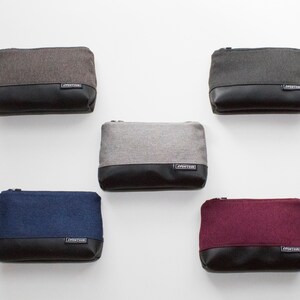 May include: Five rectangular pouches in various colors: gray, dark gray, navy blue, and burgundy. Each pouch has a textured fabric upper and a black leather-like bottom. A small label with text is on the bottom of each pouch.