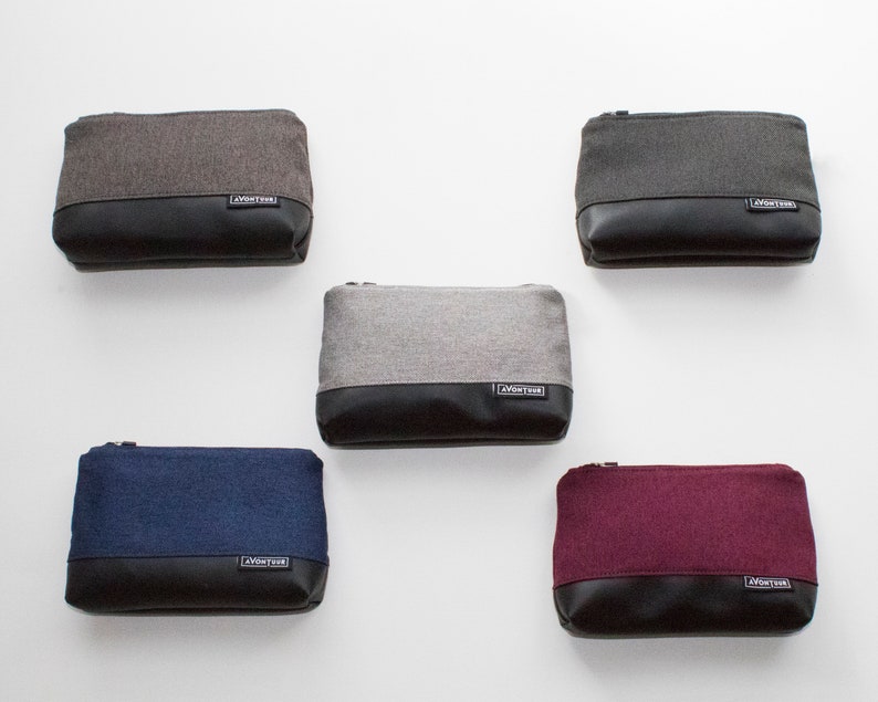 May include: Five rectangular pouches in various colors: gray, dark gray, navy blue, and burgundy. Each pouch has a textured fabric upper and a black leather-like bottom. A small label with text is on the bottom of each pouch.