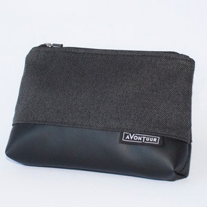 May include: A rectangular, two-toned pouch with a zipper closure. The top half is a dark gray woven fabric, and the bottom half is black faux leather. The label "AVONTUUR" is visible on the lower right.