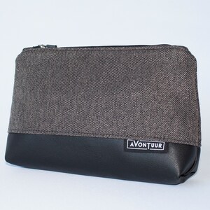 May include: A rectangular pouch with a black leather bottom and a gray fabric top. The pouch has a black zipper and a small white label with the word "AVONTUUR" on it.