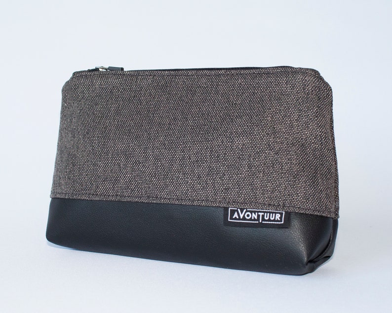 May include: A rectangular pouch with a black leather bottom and a gray fabric top. The pouch has a black zipper and a small white label with the word "AVONTUUR" on it.