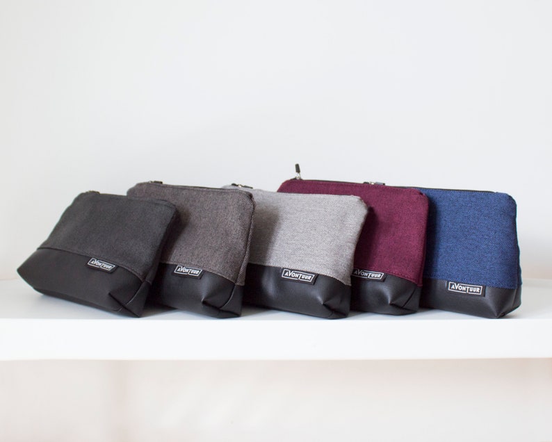 May include: A collection of five zippered pouches in various colors: black, gray, light gray, burgundy, and blue. Each pouch has a black leather-like bottom and a fabric top. The brand name "AVONTUR" is printed on a small white label.