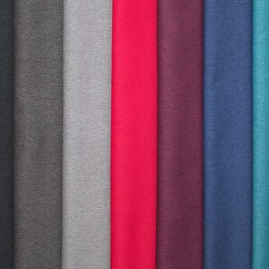 May include: A collection of fabric swatches in various colors, including black, gray, red, purple, blue, and teal. The fabric appears to be a smooth, solid material, possibly for apparel or home decor.