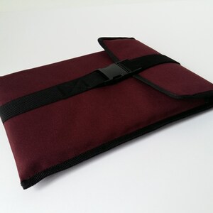 May include: A burgundy laptop sleeve with a black strap and buckle closure.