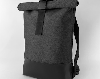 Pode incluir: Uma mochila cinza escuro com fecho enrolável e fivela preta. A seção inferior é feita de material preto liso. A mochila tem alças ajustáveis.