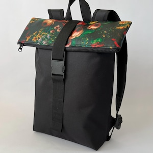 Puede incluir: Una mochila negra con cierre enrollable y un estampado floral en tonos rojos, amarillos y verdes. La bolsa incluye una correa de nailon negra con hebilla de plástico, un asa superior y correas ajustables para los hombros para su transporte.