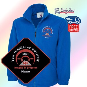 K&ouml;nnte beinhalten: Eine k&ouml;nigsblaue Fleecejacke mit durchgehendem Rei&szlig;verschluss und hohem Kragen. Die Jacke hat ein gesticktes Design mit dem Text "Your Hospital or University MRI Imaging in progress Name". Die Jacke hat auch den Text "Dirty Bear Embroidery & Workwear".