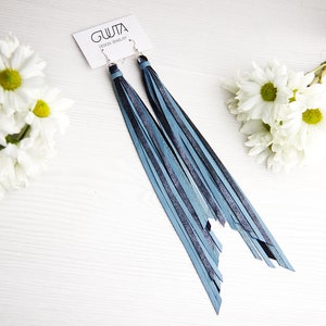 May include: A pair of long, blue and black leather fringe earrings. The earrings are hanging from silver hooks.