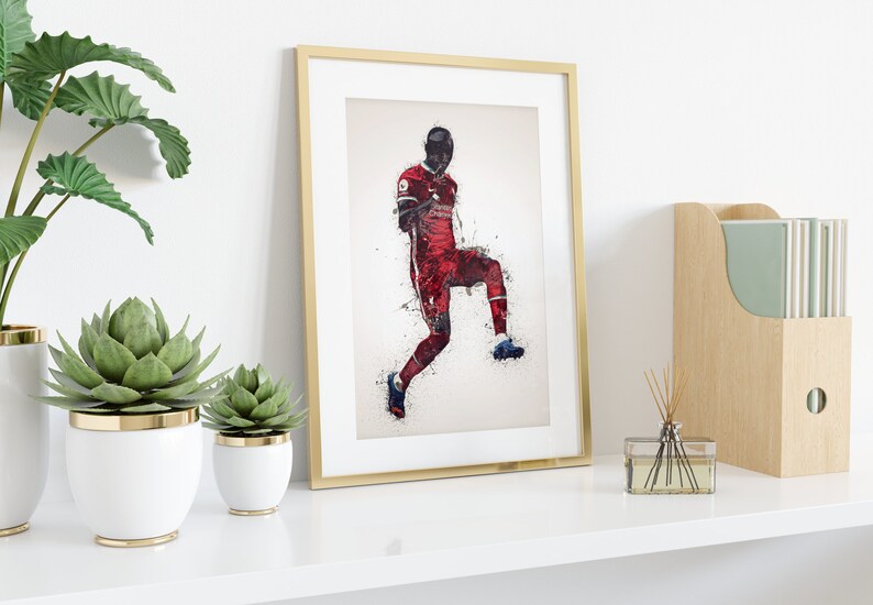 May include: A framed print of a soccer player in a red and white uniform, with a white background and a splash of color effect. The player is in mid-air, kicking the ball.