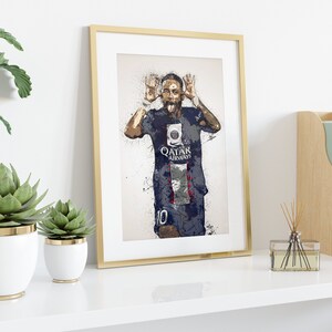 Op de afbeelding: Een ingelijste print van een voetballer in een blauw-wit shirt met de tekst "QATAR AIRWAYS" op de voorkant. De voetballer maakt een grappig gezicht met zijn tong naar buiten. De print is omgeven door een gouden lijst.