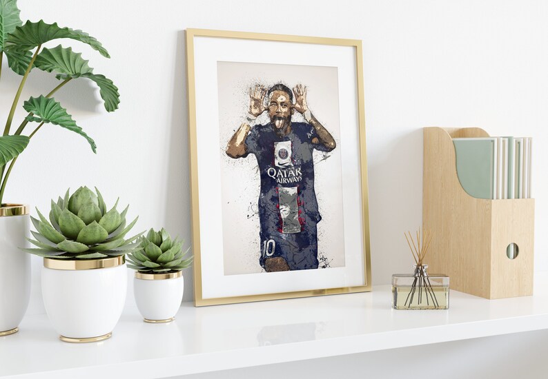 Op de afbeelding: Een ingelijste print van een voetballer in een blauw-wit shirt met de tekst "QATAR AIRWAYS" op de voorkant. De voetballer maakt een grappig gezicht met zijn tong naar buiten. De print is omgeven door een gouden lijst.