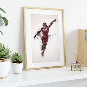 May include: A framed print of a soccer player in a red and black uniform, celebrating a goal with a raised arm and a splash of paint behind them.