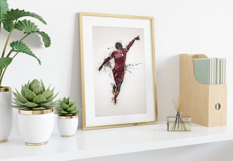 May include: A framed print of a soccer player in a red and black uniform, celebrating a goal with a raised arm and a splash of paint behind them.