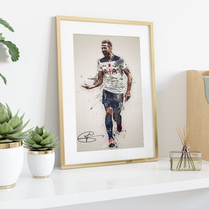 May include: A framed print of a football player in a white shirt with a blue and white pattern, running with the ball. The player's shirt has the text "AIA" on the front. The print has a gold frame and is on a white shelf with plants and a wooden box.
