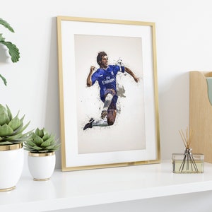 May include: A framed print of a soccer player in a blue jersey with white accents, running with the ball. The jersey has the text "Fly Emirates" on the front. The background is a white and gray abstract design.