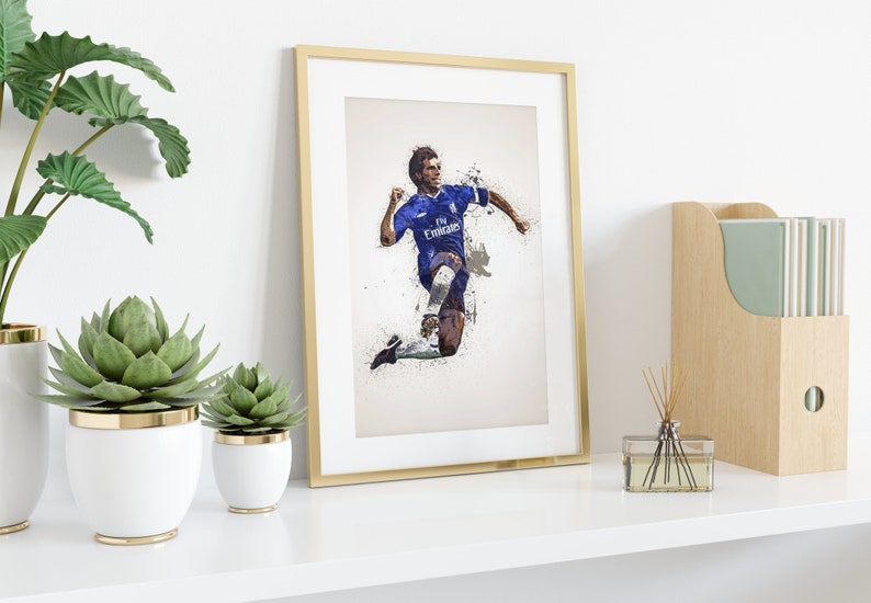 May include: A framed print of a soccer player in a blue jersey with white accents, running with the ball. The jersey has the text "Fly Emirates" on the front. The background is a white and gray abstract design.