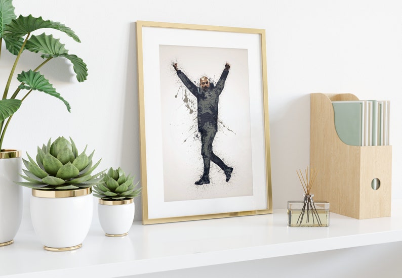 May include: A framed print of a black and white illustration of a person with arms raised in the air, standing on a white background with black paint splatters.