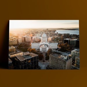 May include: An aerial view of a city with a large white building in the center. The building has a dome and is surrounded by other buildings. The city is bathed in the golden light of the setting sun.