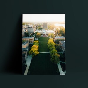 May include: Aerial view of a university campus with a large green lawn surrounded by buildings. The lawn is lined with trees and walkways. The buildings are brick and have a traditional architectural style.