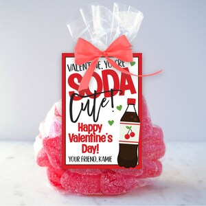 Peut inclure: Un sac en cellophane transparent rempli de bonbons g&eacute;lifi&eacute;s roses, nou&eacute; avec un n&oelig;ud rouge. Une &eacute;tiquette rectangulaire indique "Valentine, you're soda cute! Happy Valentine's Day!" avec une illustration de bouteille de soda.