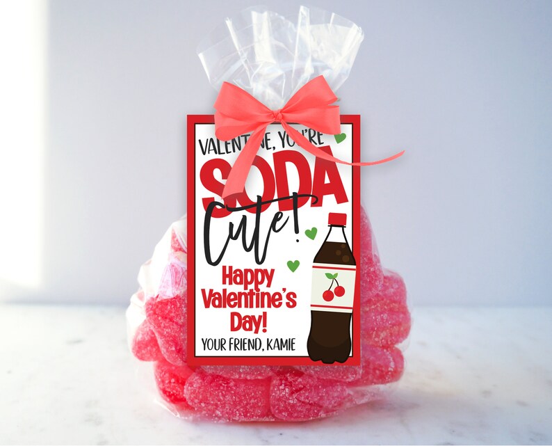 Peut inclure: Un sac en cellophane transparent rempli de bonbons g&eacute;lifi&eacute;s roses, nou&eacute; avec un n&oelig;ud rouge. Une &eacute;tiquette rectangulaire indique "Valentine, you're soda cute! Happy Valentine's Day!" avec une illustration de bouteille de soda.
