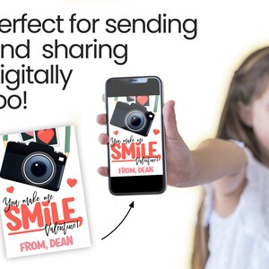 Peut inclure: Une carte de Saint-Valentin et un smartphone affichant un design similaire. La carte et l'&eacute;cran du t&eacute;l&eacute;phone pr&eacute;sentent un appareil photo noir, des coeurs rouges et le texte "You make me SMILE Valentine! FROM, DEAN."
