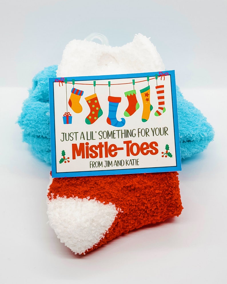 May include: A pair of red and white fuzzy socks with a tag that says "Just a lil' something for your Mistle-Toes from Jim and Katie". The tag has a blue background with a picture of five Christmas stockings hanging from a clothesline.
