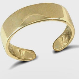 Könnte beinhalten: Ein goldfarbener, offener Ring. Der Ring hat eine glatte, polierte Oberfläche und ein geschwungenes Design. Die offenen Enden ermöglichen eine verstellbare Größe. Der Ring ist wahrscheinlich aus Metall und soll an einem Finger oder Zeh getragen werden.