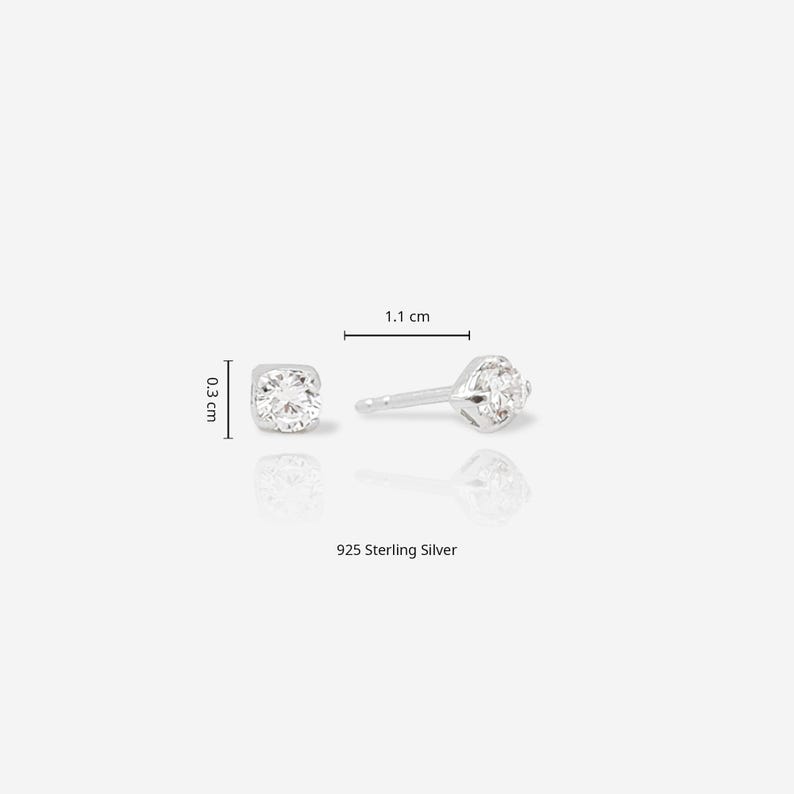 May include: A pair of 925 sterling silver stud earrings featuring a clear round gemstone. The earrings measure 0.3 cm in diameter and 1.1 cm in length, as indicated by the visible measurement lines and text labels included in the image.