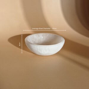 May include: A white, translucent, circular bowl with a smooth, polished finish. The bowl has an average diameter of 10 cm and a height of 4 cm, as indicated by the text and measurement lines visible in the image.