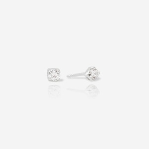 May include: A pair of silver stud earrings featuring a single round, clear, faceted gemstone set in a four-prong metal setting. One earring is shown from the front, while the other is positioned to display the post and the side profile of the setting.