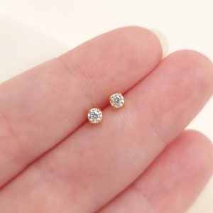 May include: A pair of small stud earrings featuring round, clear, faceted stones set in yellow gold prongs. Each earring has a single brilliant-cut stone held securely by four metal prongs, creating a classic and simple design for everyday wear.