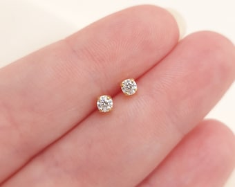 May include: A pair of small stud earrings featuring round, clear, faceted stones set in yellow gold prongs. Each earring has a single brilliant-cut stone held securely by four metal prongs, creating a classic and simple design for everyday wear.