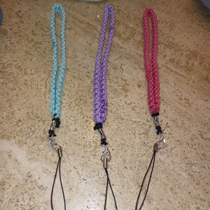 May include: Three phone straps with silver clasps and black lanyards. The straps are made of braided cord in light blue, purple, and pink.
