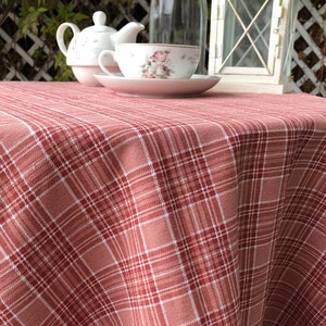 May include: A red and white plaid tablecloth with a subtle sheen. The tablecloth is draped over a round table and has a slightly wrinkled appearance.