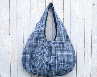 May include: A blue and black plaid tote bag with a black lining. The bag is hanging on a white wooden wall.