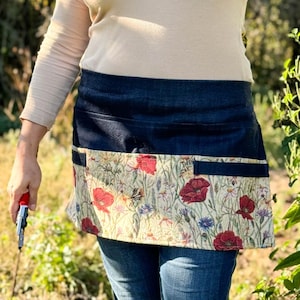 May include: A denim and floral gardening apron with multiple pockets. The apron is worn over a beige long-sleeved shirt.