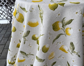 May include: A round tablecloth with a lemon pattern. The fabric is a light beige color, and the lemons are yellow and green with white flowers and green leaves. The tablecloth is draped over a round table.