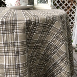 Puede incluir: Un mantel redondo con un patrón de cuadros marrones y blancos. El mantel está hecho de un tejido suave y tejido, perfecto para un comedor informal.
